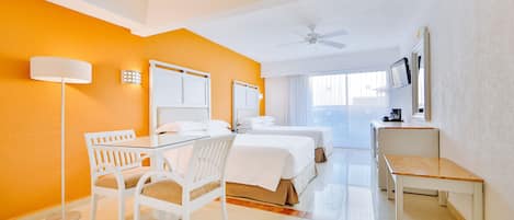 A hotel room with two beds, a desk, a chair, a lamp, and a ceiling fan.