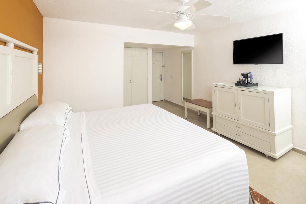 Un dormitorio con una cama grande, un armario, un escritorio y un televisor en la pared.