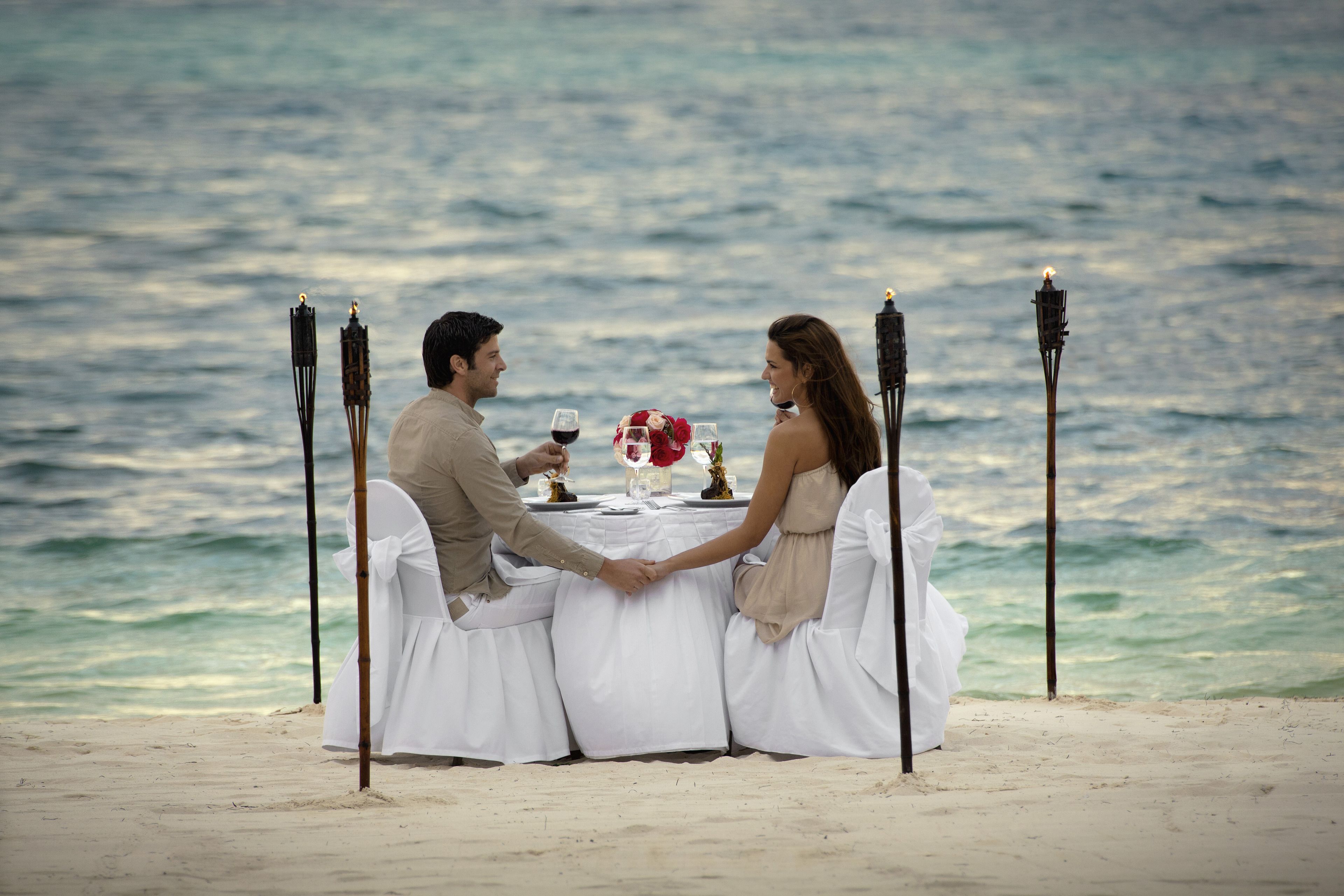 A couple dining at a table on a beach with ocean views.