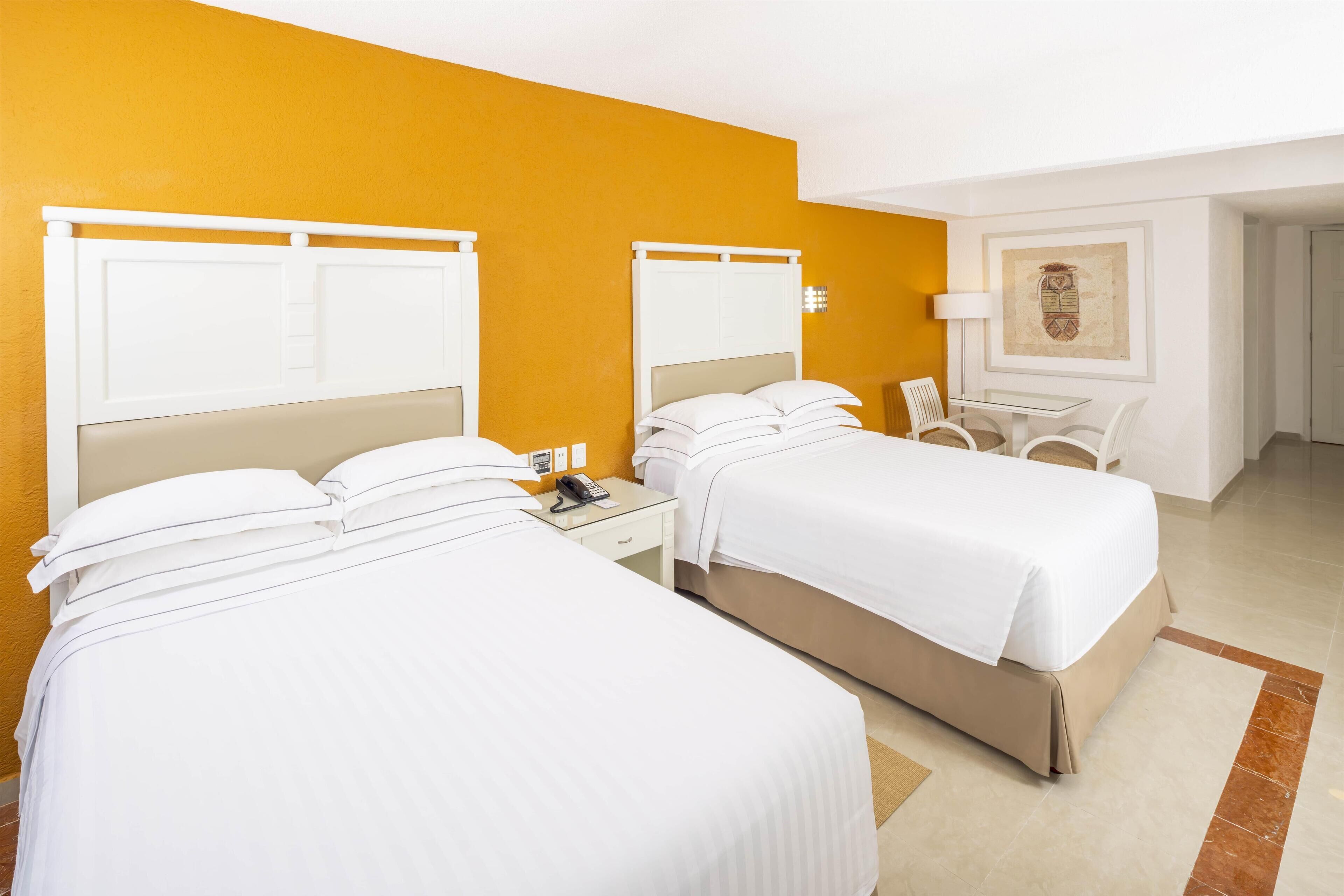 A hotel room with two beds, a small table, a chair, and a lamp.