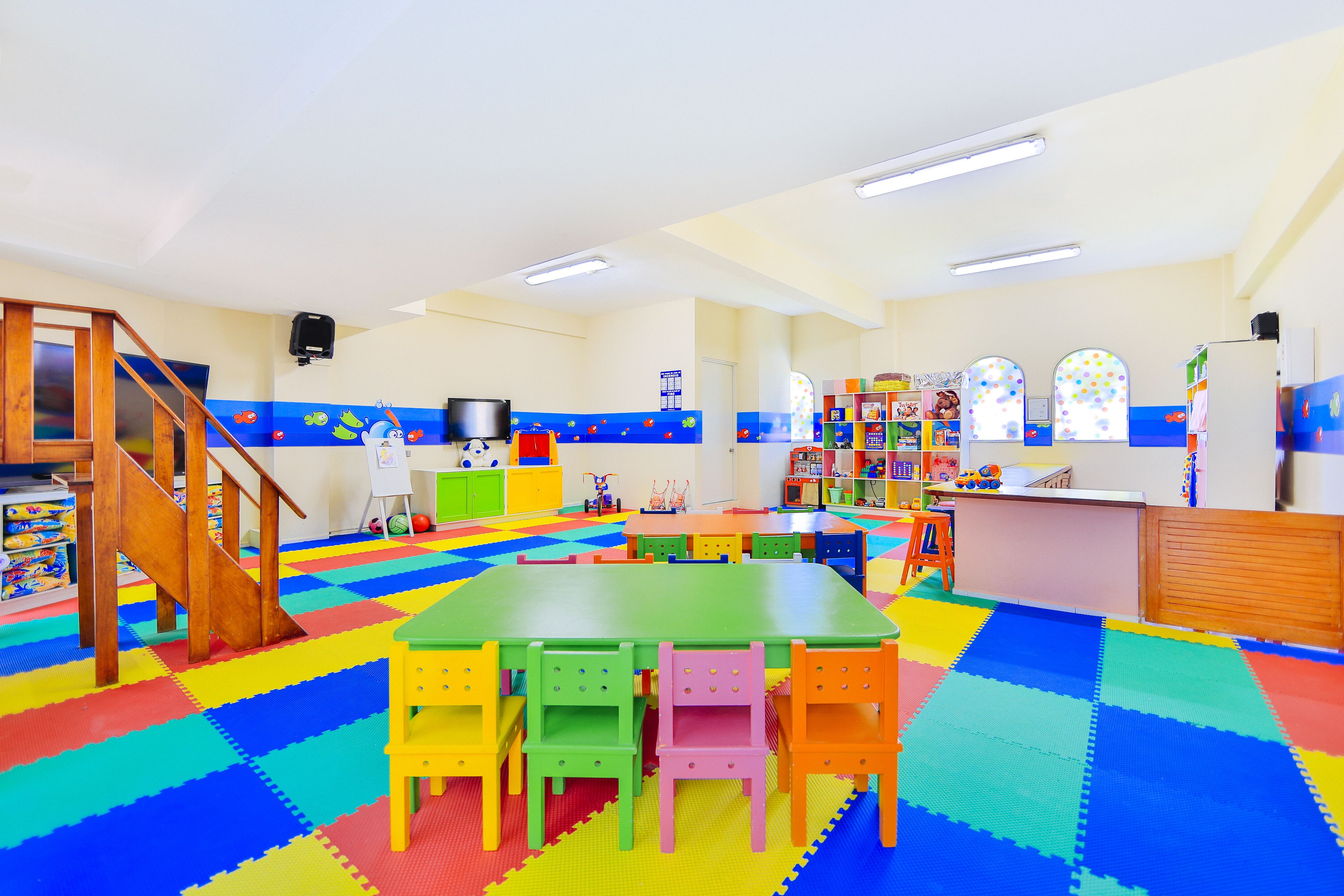 Una sala de juegos luminosa con tapetes coloridos, una mesa verde y sillas.