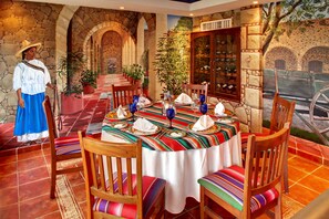A restaurant with a stone archway entrance, wooden chairs with colorful cushions, and a table set with blue glassware and plates. - Occidental Costa Cancún All Inclusive (Cancun)