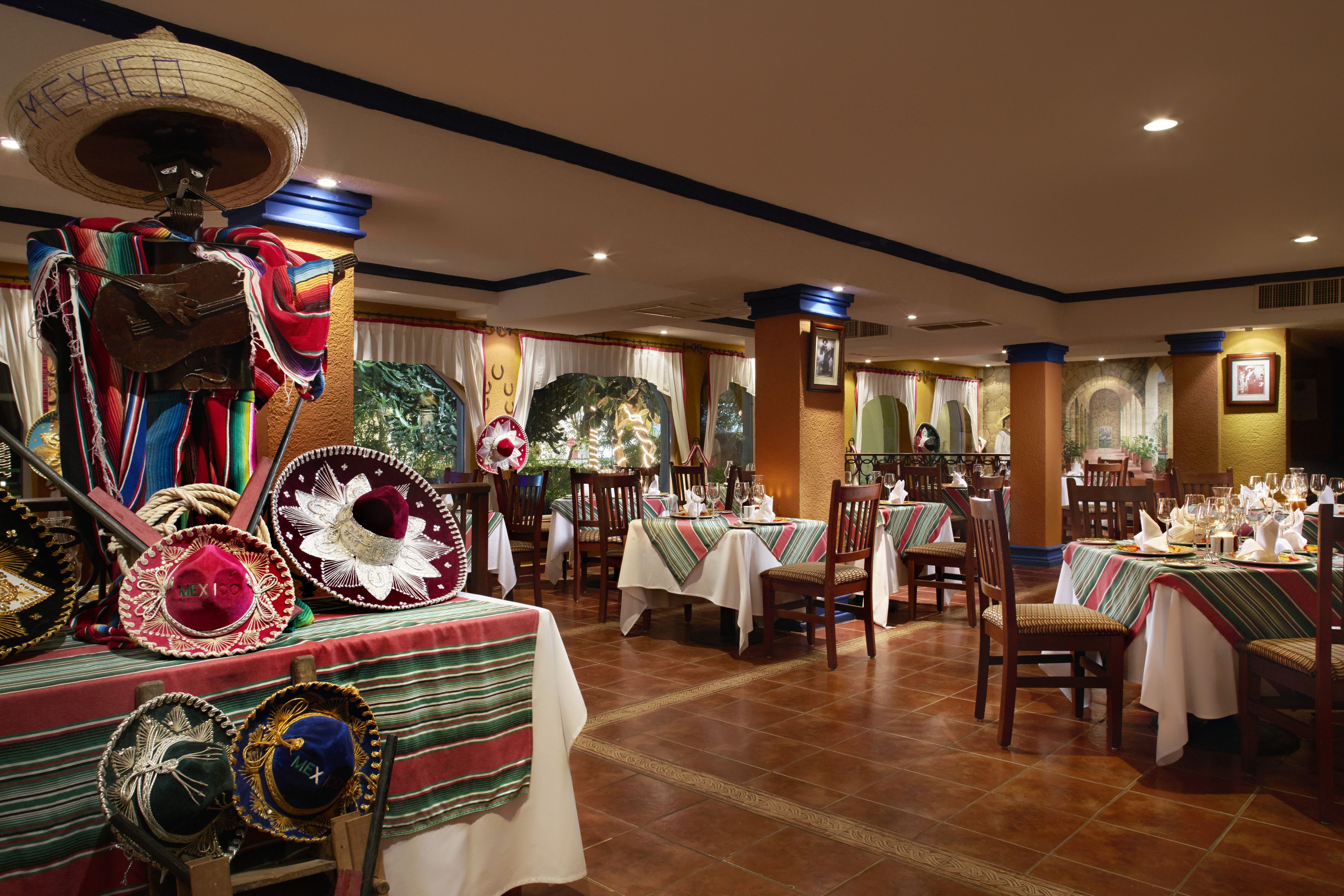 A restaurant with tables set for dining, decorated with traditional Mexican hats and textiles.