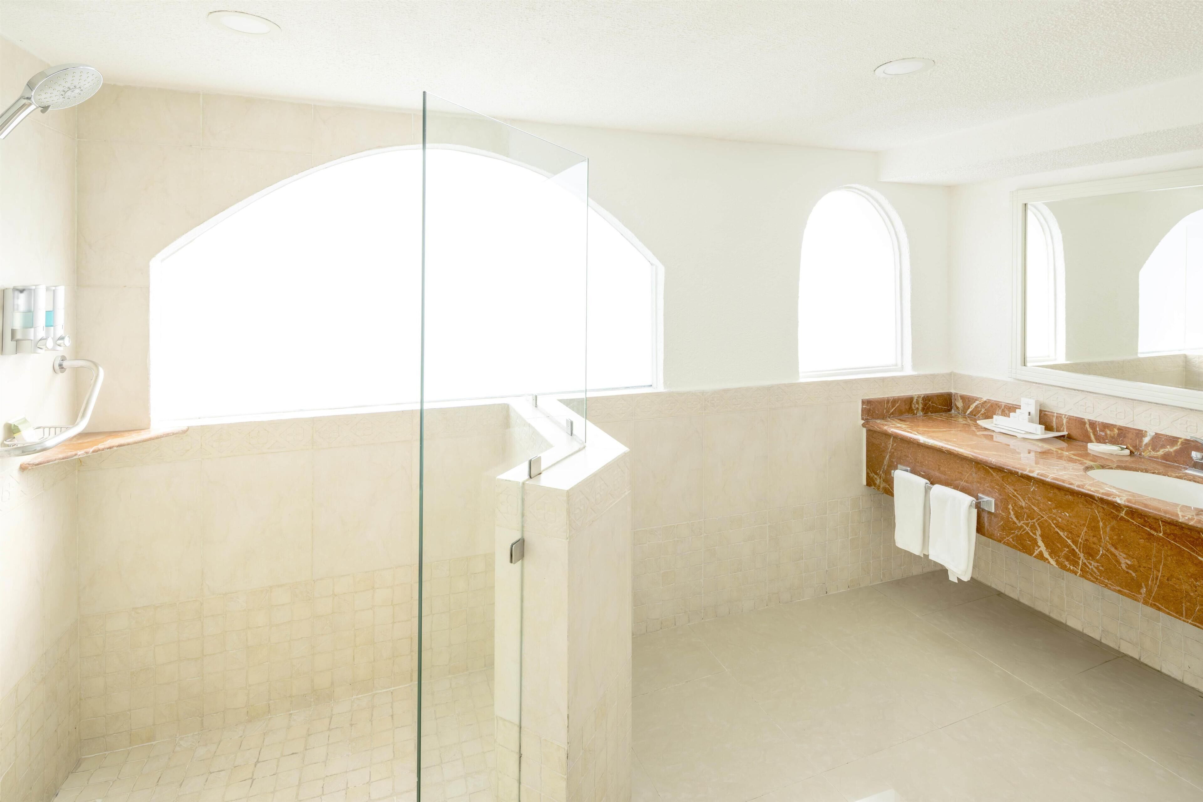 A modern bathroom with a glass shower enclosure, a marble vanity, and large arched windows.