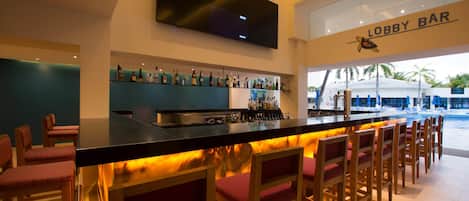 A bar area with a flat-screen TV mounted above the bar, a bar counter with a warm backlight, and a sign reading "Lobby Bar".