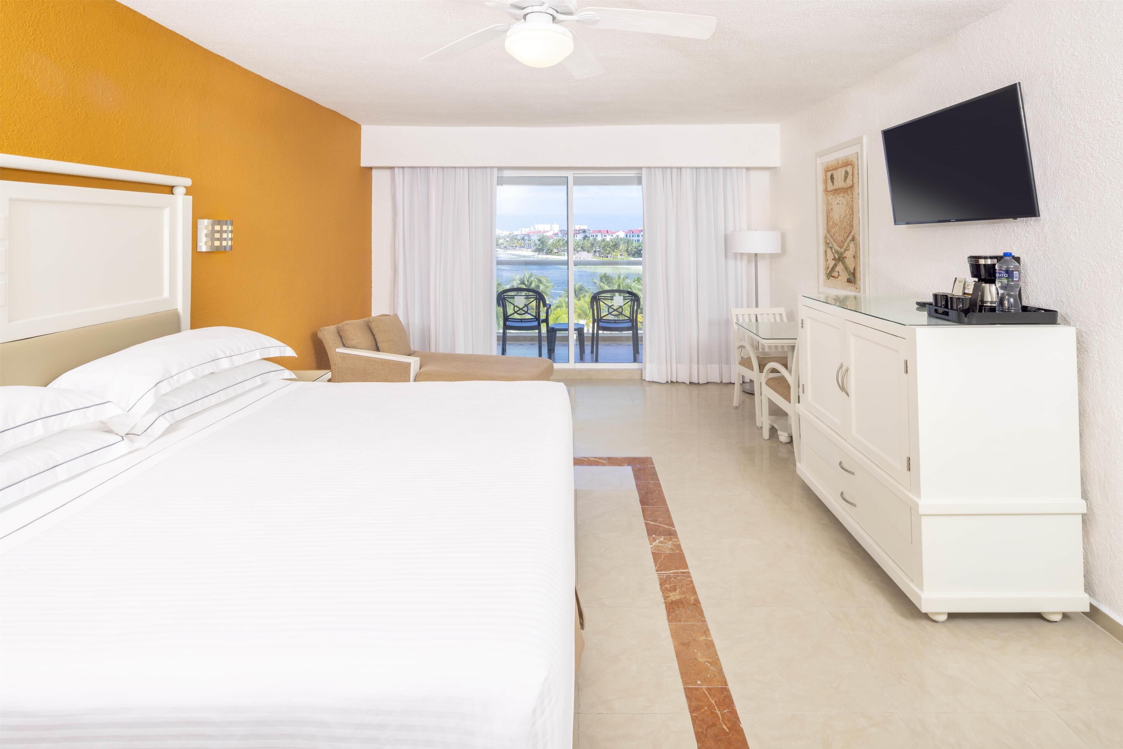 A hotel room with a bed, a chair, a desk, a TV, and a balcony with a view.