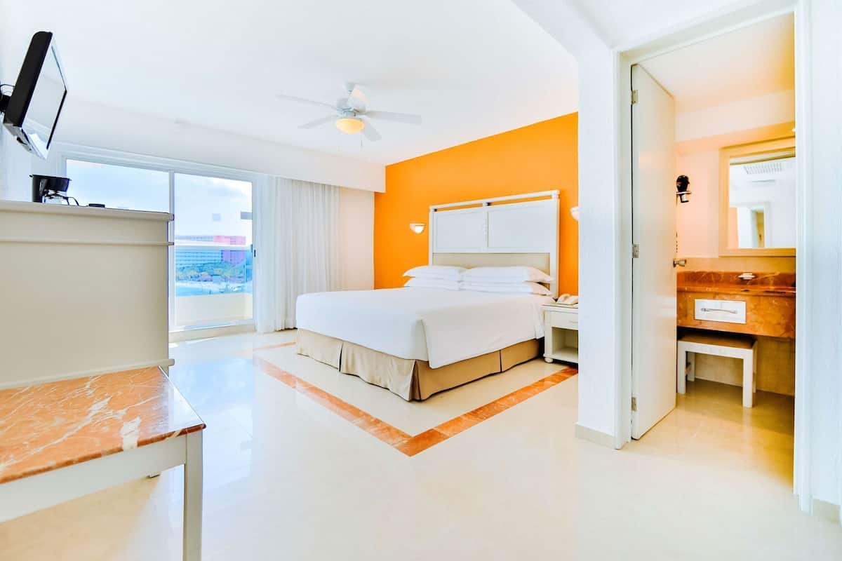 Habitación de hotel moderna con cama, escritorio, silla, mesita de noche, espejo y ventilador de techo.