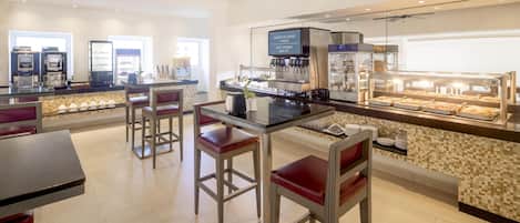 A modern bar area with a coffee machine, a beverage dispenser, and a display case with pastries.
