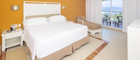 A hotel room with a large bed, a desk with a phone, a chair, and a view of the ocean through a balcony.