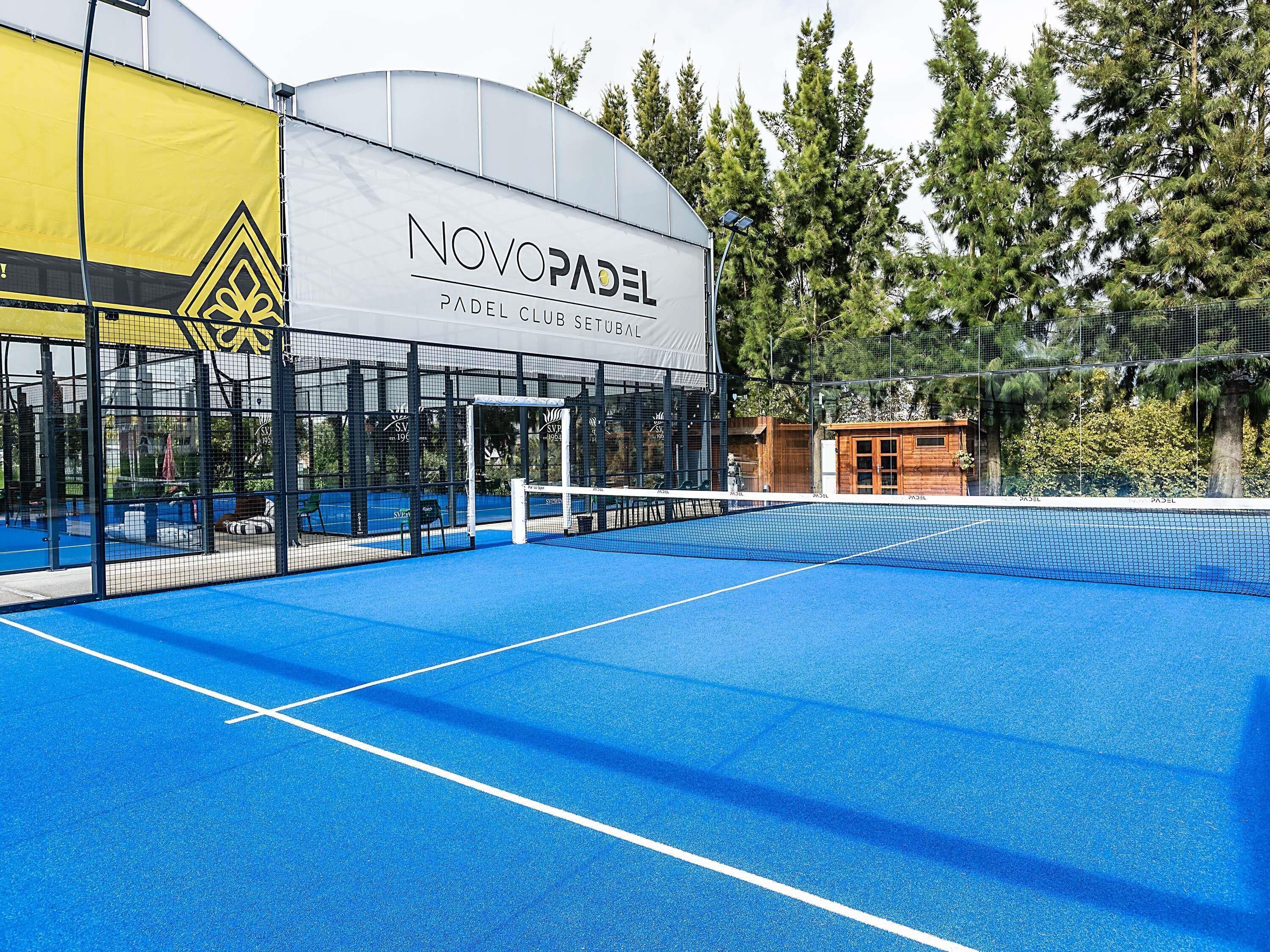Een tennisbaan met een net, omgeven door een hek en bomen.