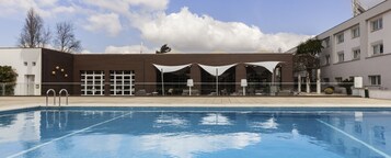 Una piscina con un edificio moderno al fondo, que cuenta con amplios ventanales y una zona de estar cubierta.