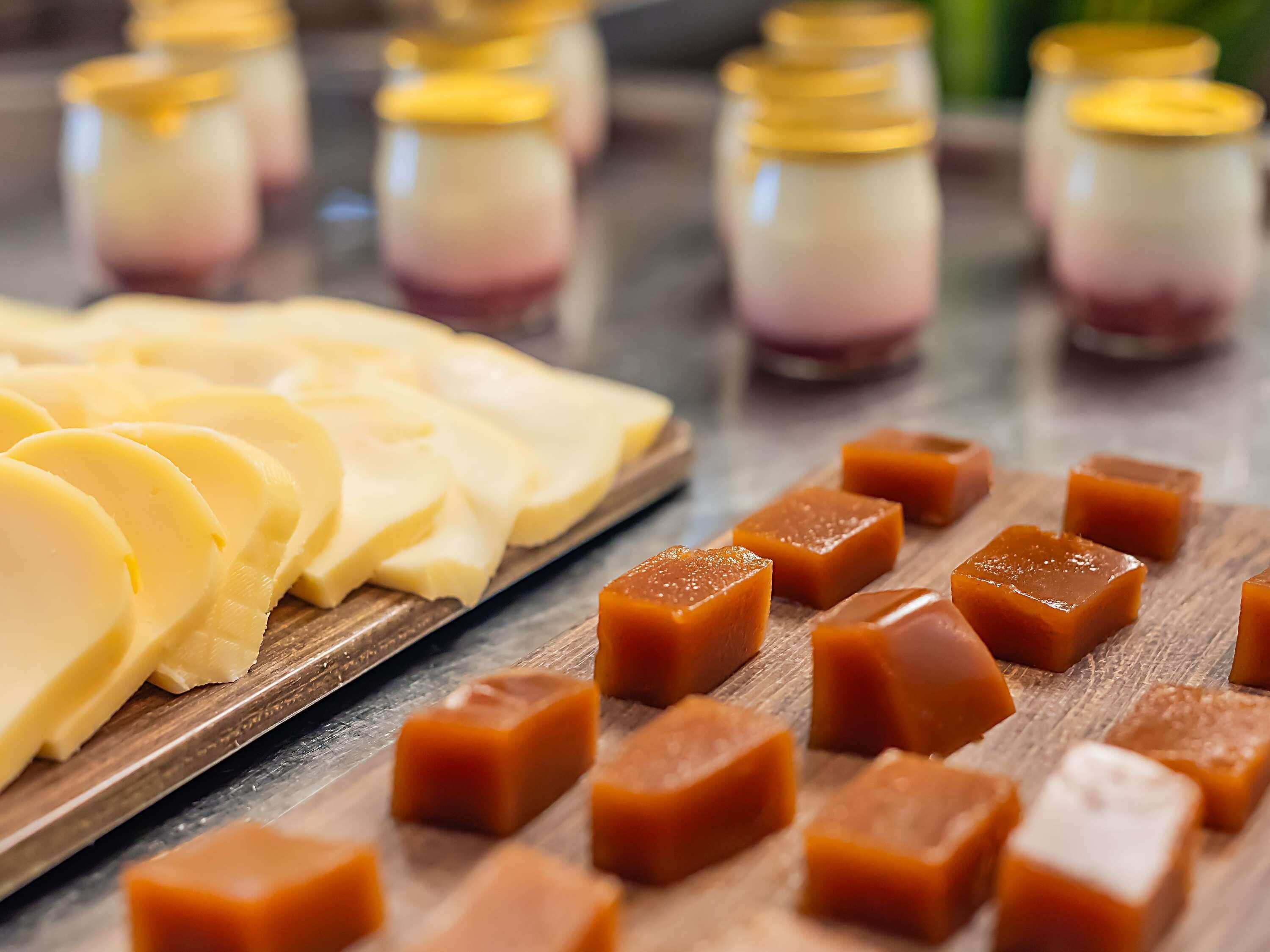 A wooden board with cheese slices and caramel cubes.