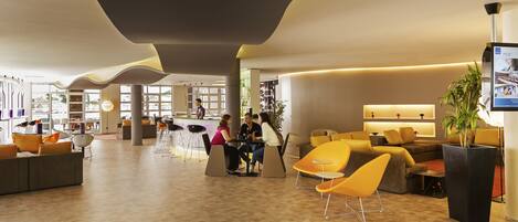 A modern lobby with a reception desk, seating areas, and a large plant.