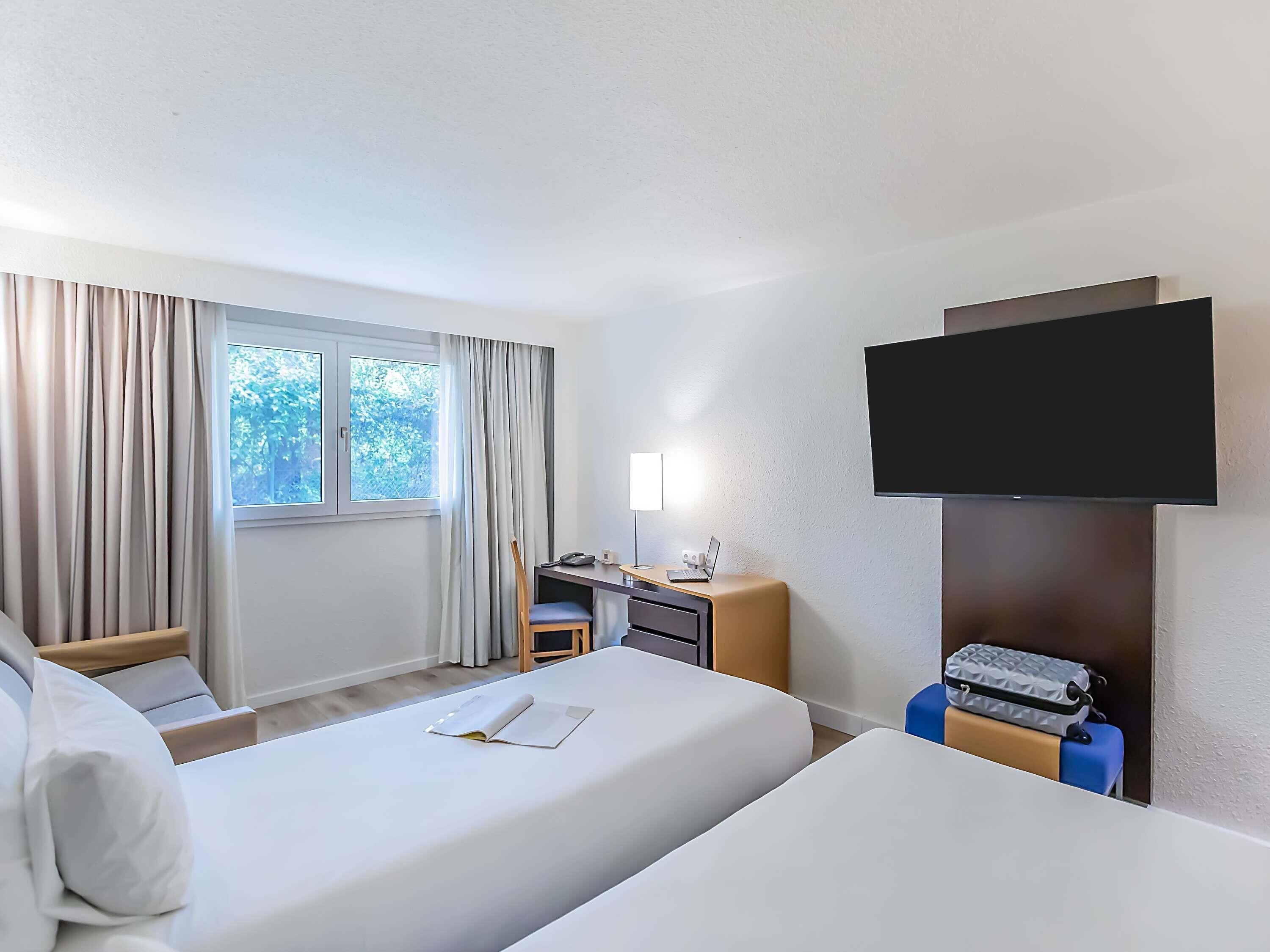 Ein Hotelzimmer mit Bett, Schreibtisch, Stuhl, Fernseher und einem Fenster mit Vorhängen.