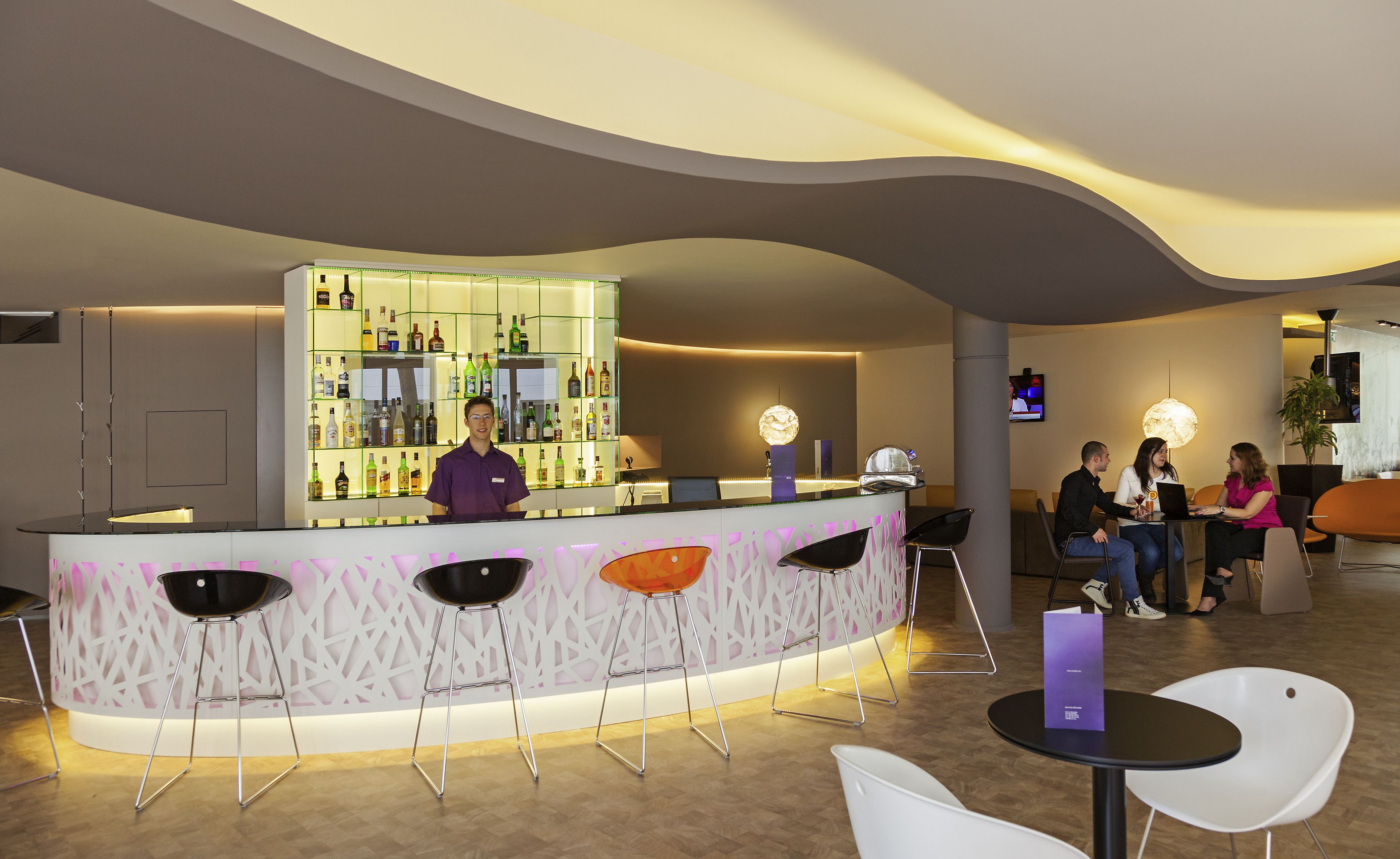 Zona de bar moderna con un cantinero, asientos con taburetes y una barra que exhibe varias botellas.