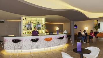 Zona de bar moderna con un cantinero, asientos con taburetes y una barra que exhibe varias botellas.