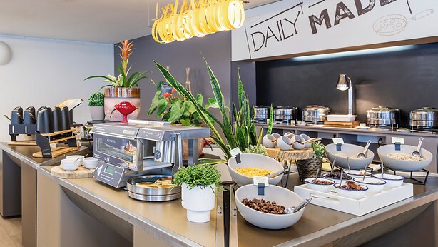 A buffet setup with various food items and a coffee machine. - Novotel Setubal (Setubal)