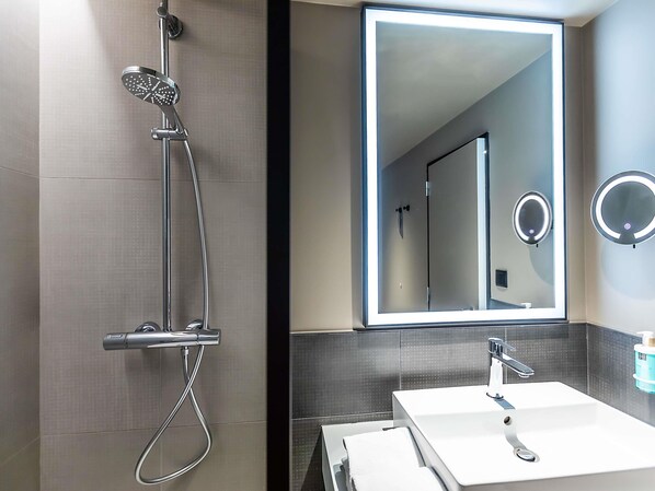 A modern bathroom with a shower, a large mirror, and a sink. - Novotel Setubal (Setubal)