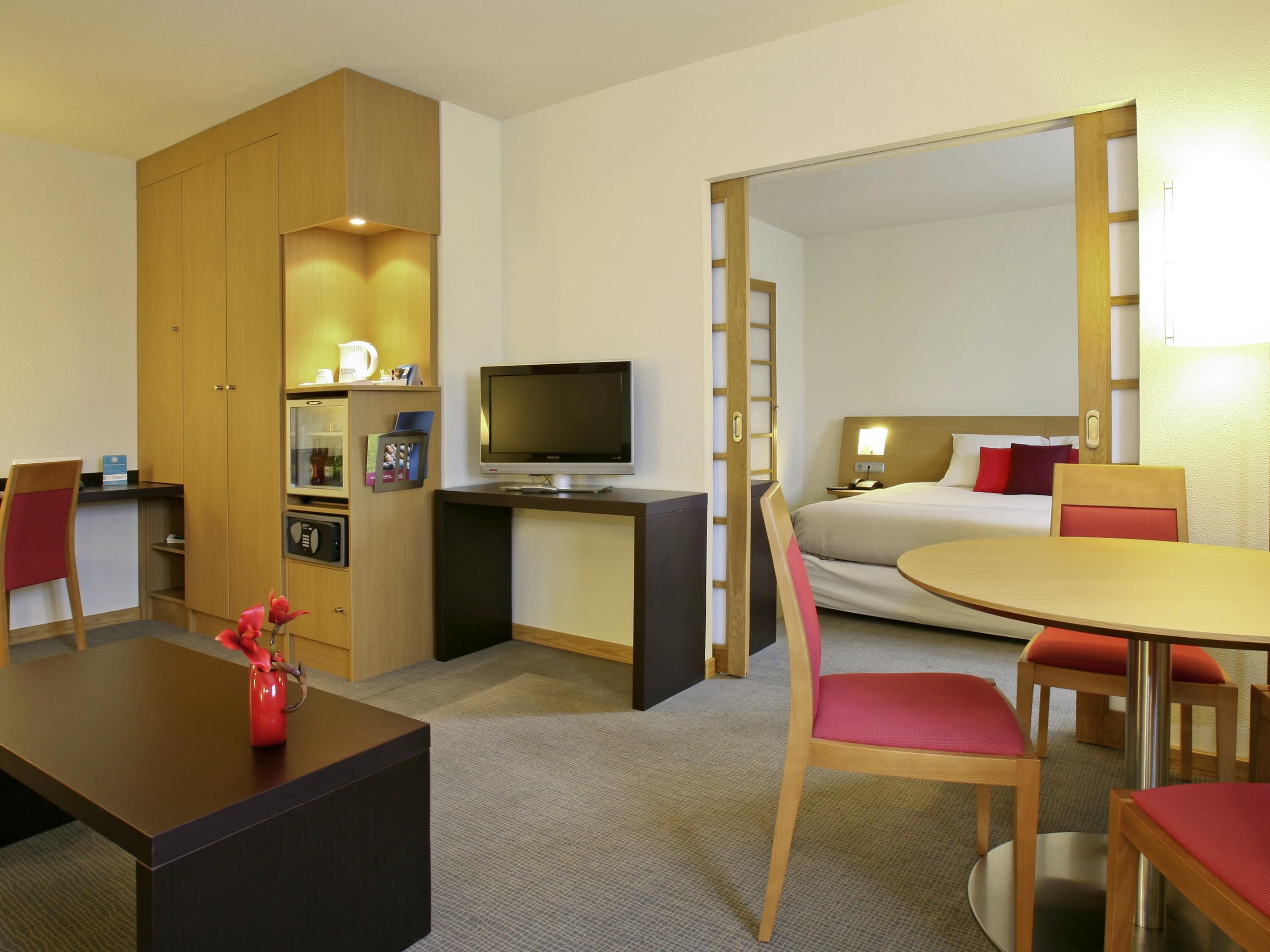 Una habitación de hotel con cama, escritorio con televisor, mesa de comedor con sillas, cafetera y armario.