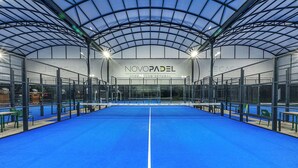 An indoor tennis court with a net, surrounded by seating areas and a covered roof structure. - Novotel Setubal (Setubal)