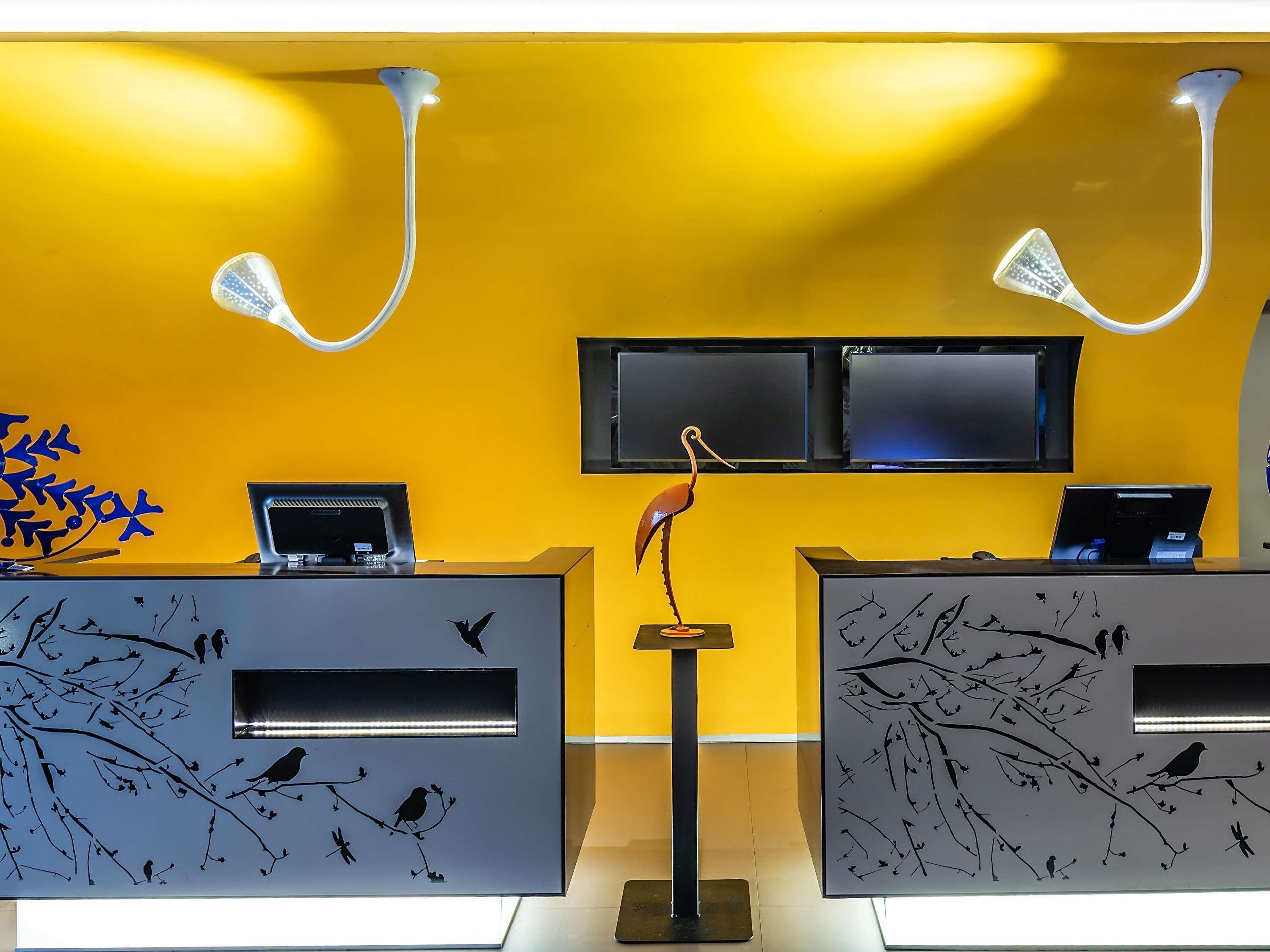 A reception desk with two monitors, a bird sculpture, and wall art depicting birds on branches.