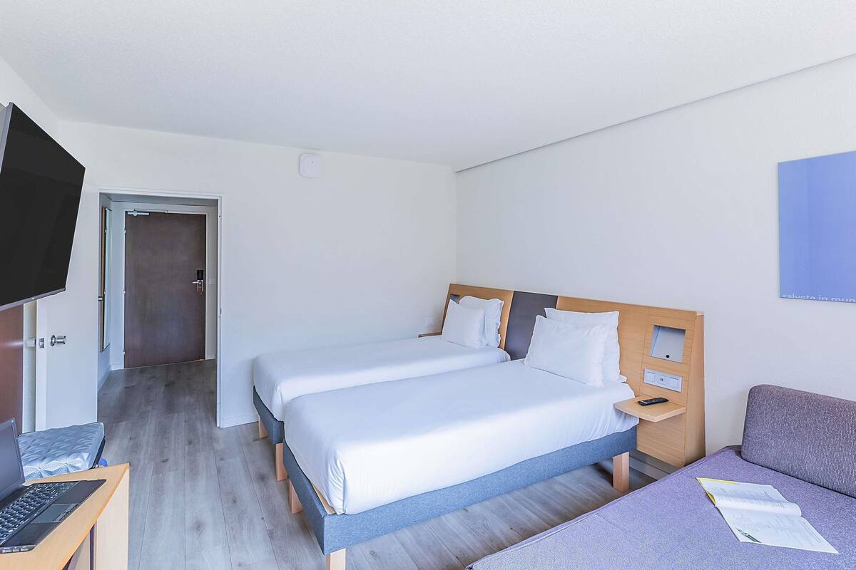 Una habitación de hotel con dos camas, un escritorio con una computadora portátil, un televisor y un sofá.