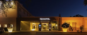 A Novotel hotel with a modern facade, illuminated signage, and large potted plants at the entrance.