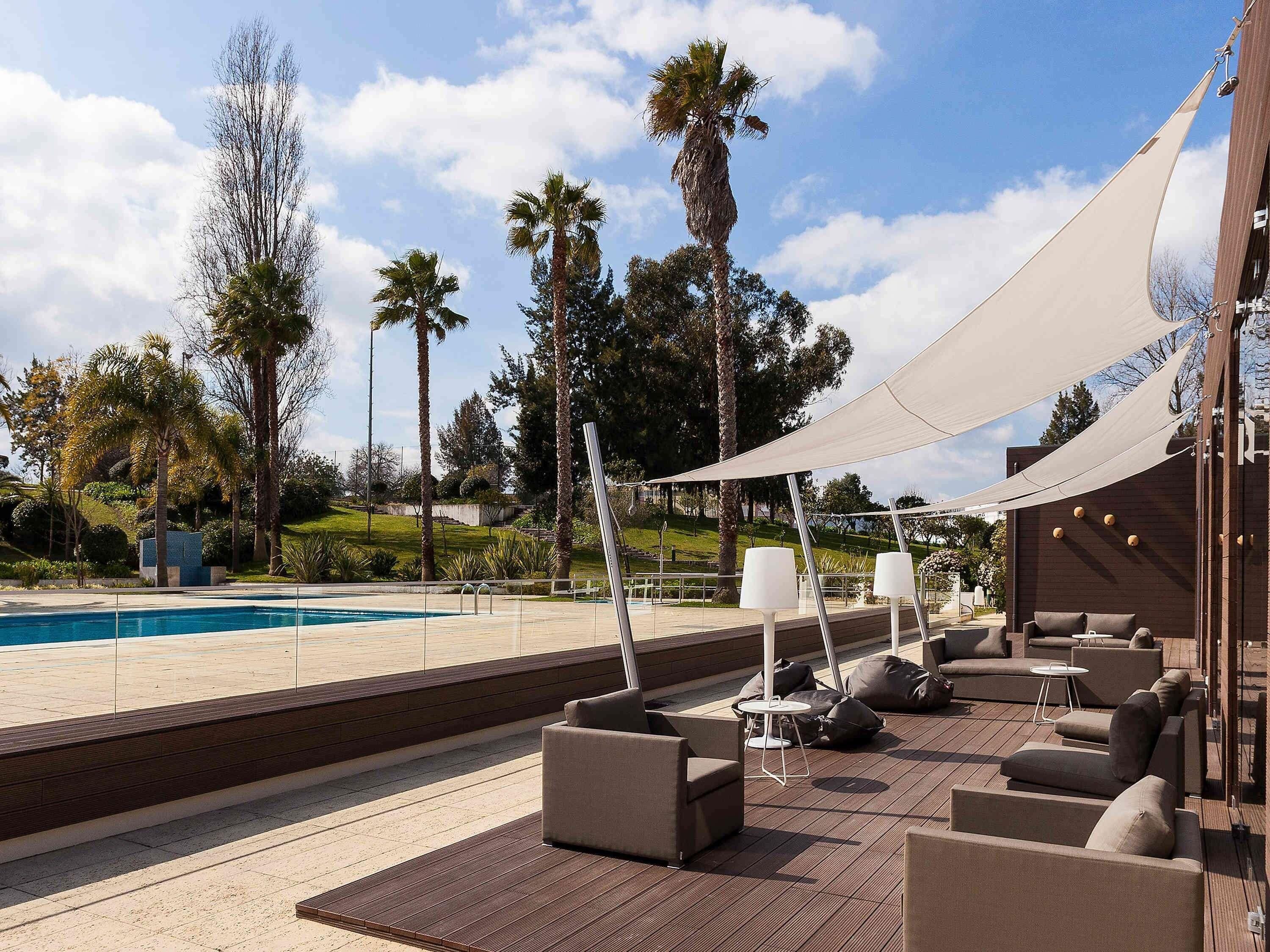 A poolside area with outdoor seating, a pool, and palm trees.