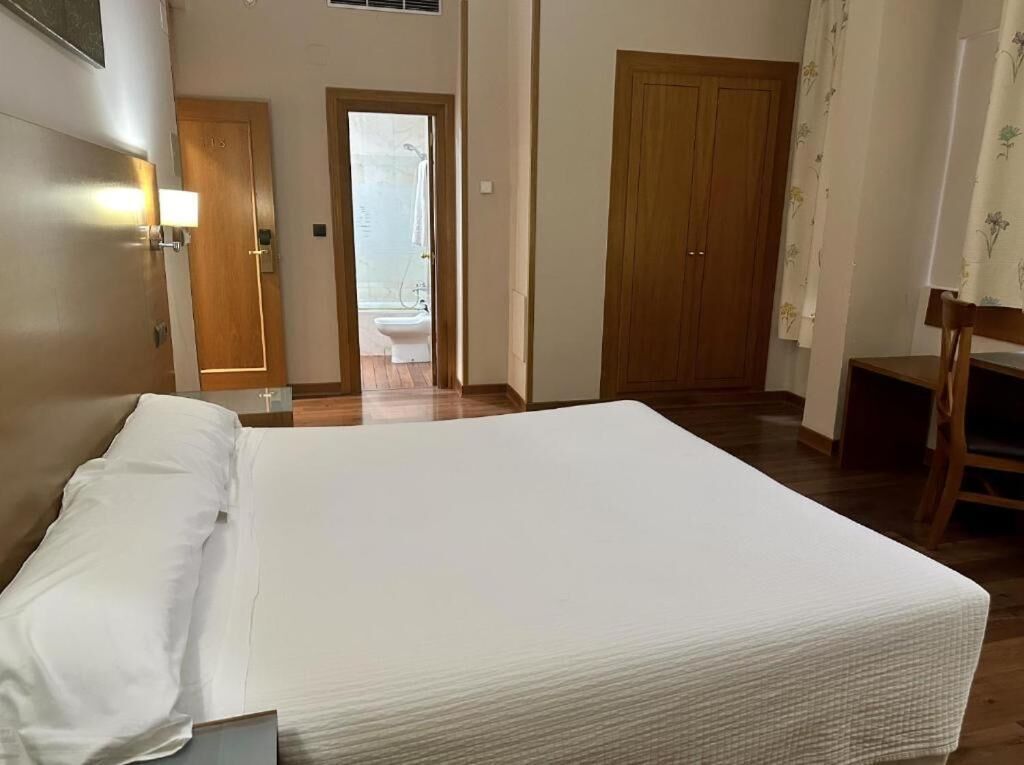 Habitación de hotel con una cama, una puerta de madera, un baño con inodoro y una silla.