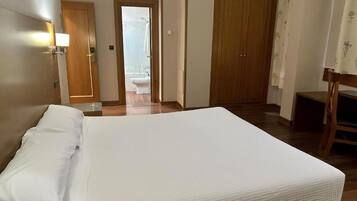 Habitación de hotel con una cama, una puerta de madera, un baño con inodoro y una silla.
