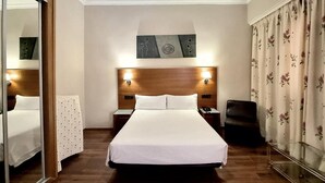 A hotel room with a bed, a nightstand, a chair, a mirror, and a painting on the wall.