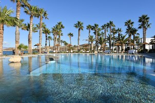 Una piscina cristalina rodeada de palmeras y sillas de descanso, con vista al mar.