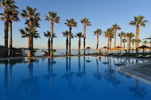 A pool with palm trees and lounge chairs, surrounded by a clear sky. - Astir Of Paros (Paros)
