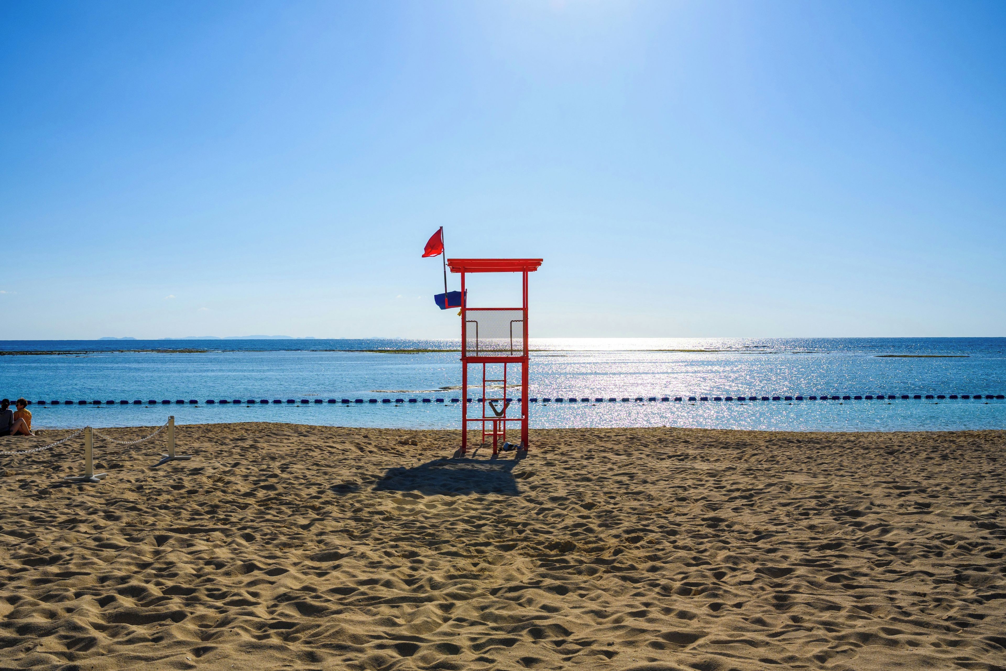 Una playa con una torre de salvavidas, cielo despejado y mar tranquilo.