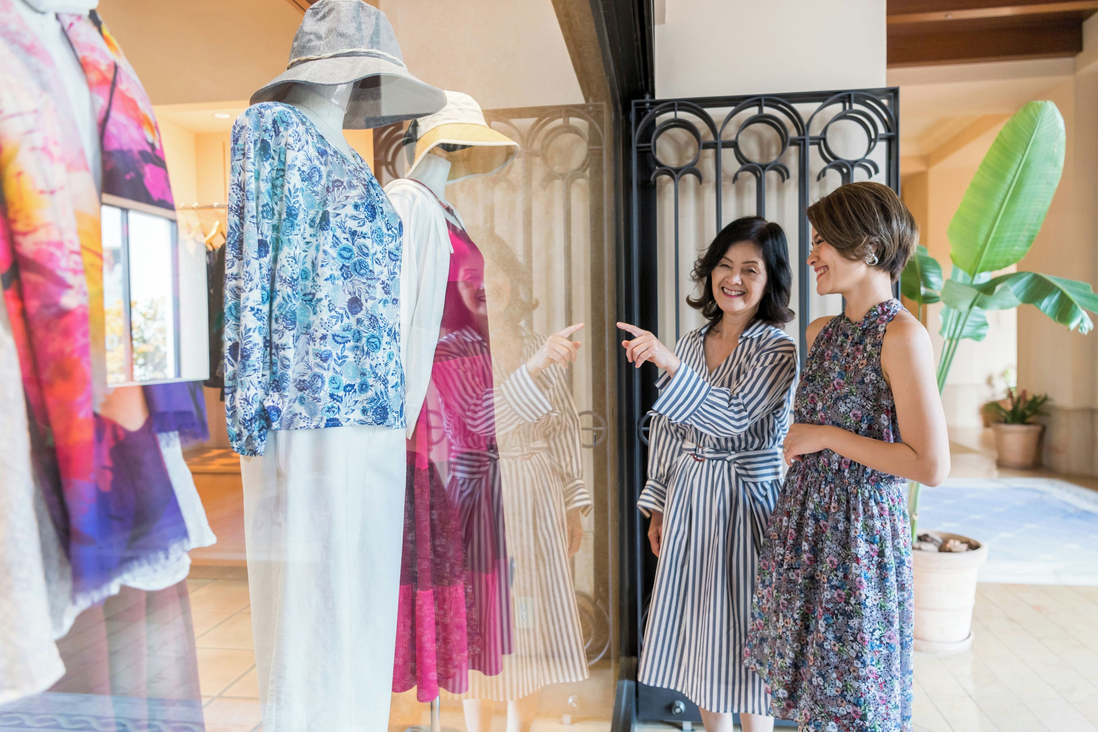 A clothing store with mannequins displaying dresses and a person examining the clothing.