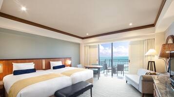 A hotel room with two beds, a desk, a chair, a sofa, a bench, and a view of the ocean.