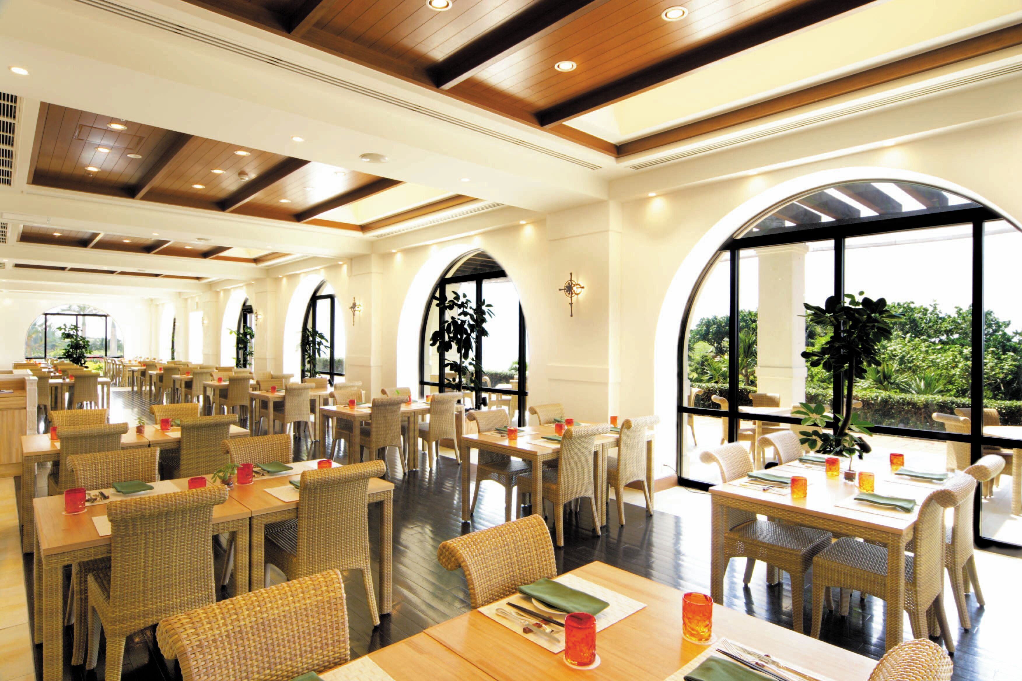 A spacious restaurant with high ceilings, arched windows, and wicker furniture.