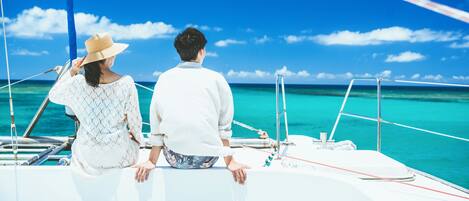 A couple on a sailboat with a clear view of the turquoise sea and sky.