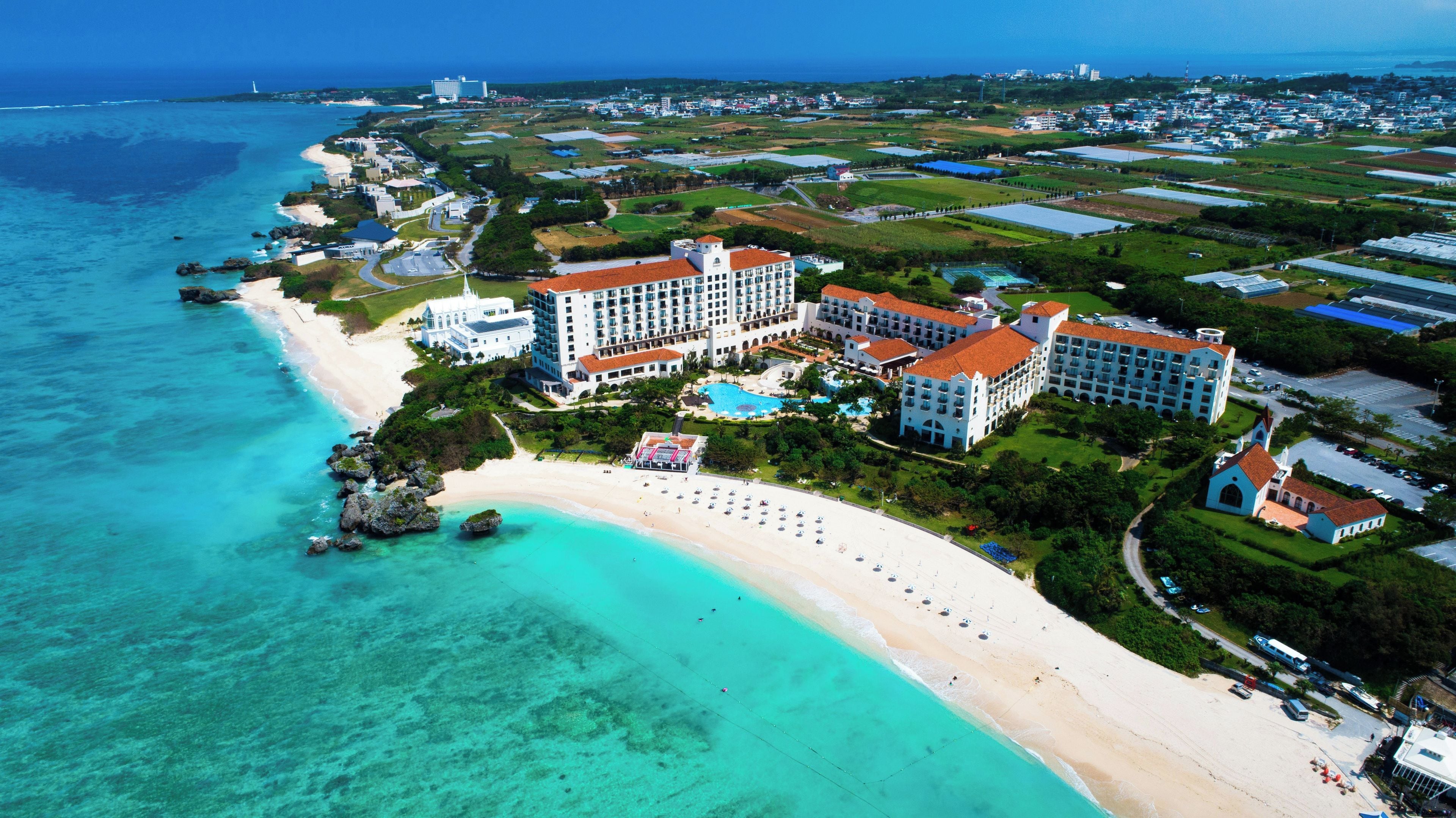 Un complejo turístico frente al mar con playa, piscina y varios edificios hoteleros.