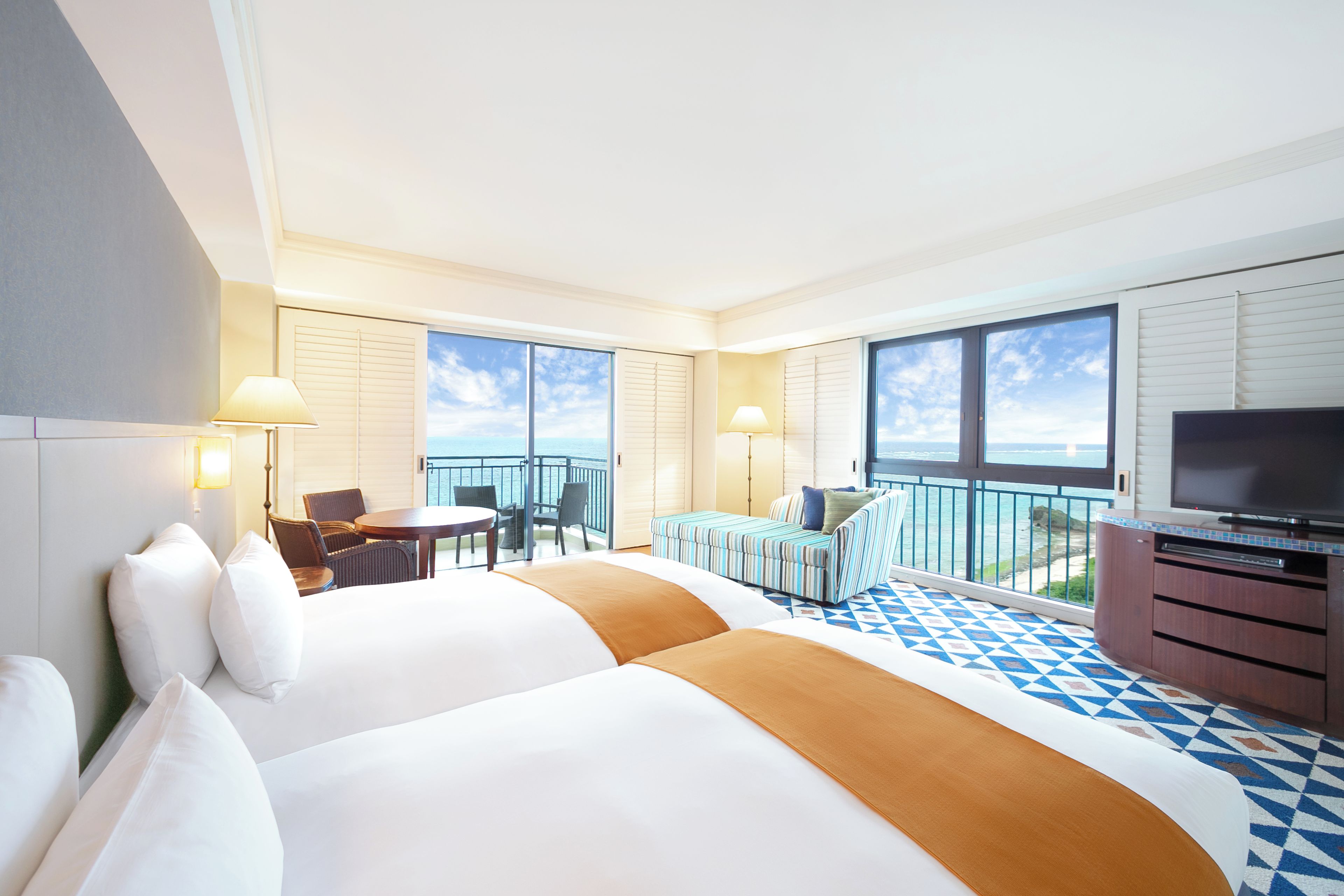 A hotel room with two beds, a balcony with a view, a TV, and a dining area.