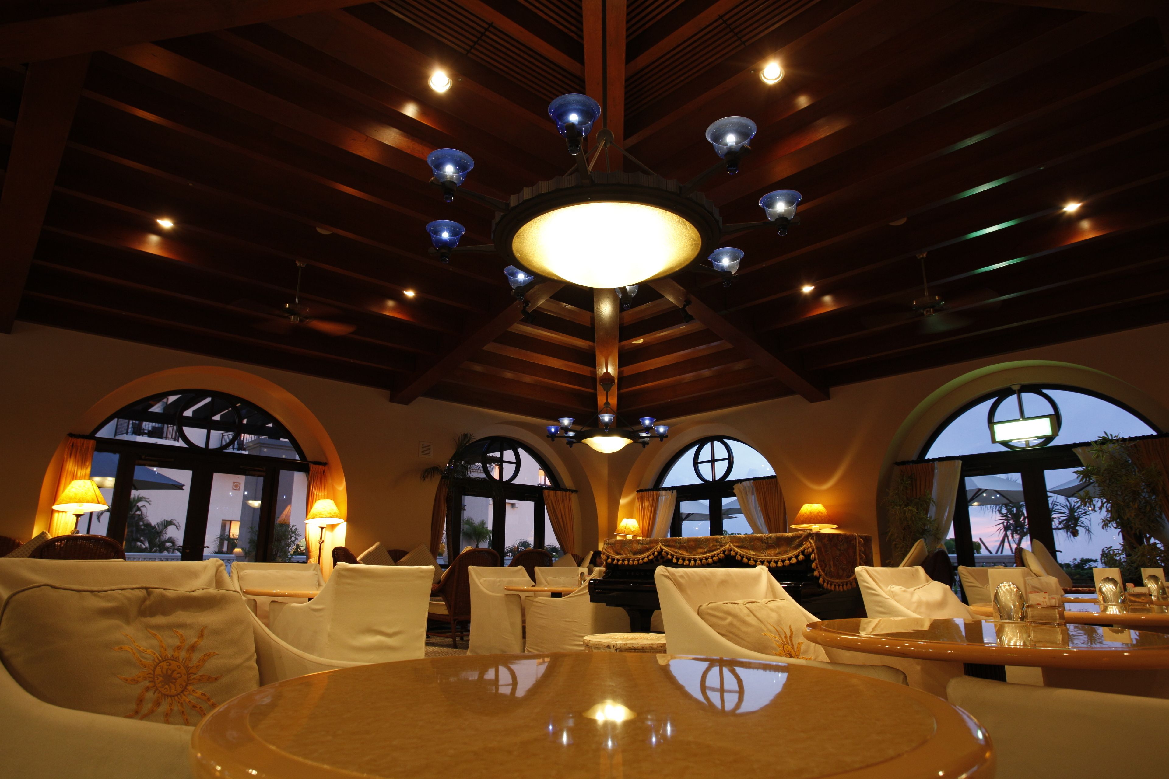 A well-lit dining area with a large chandelier, arched windows, and white furniture.