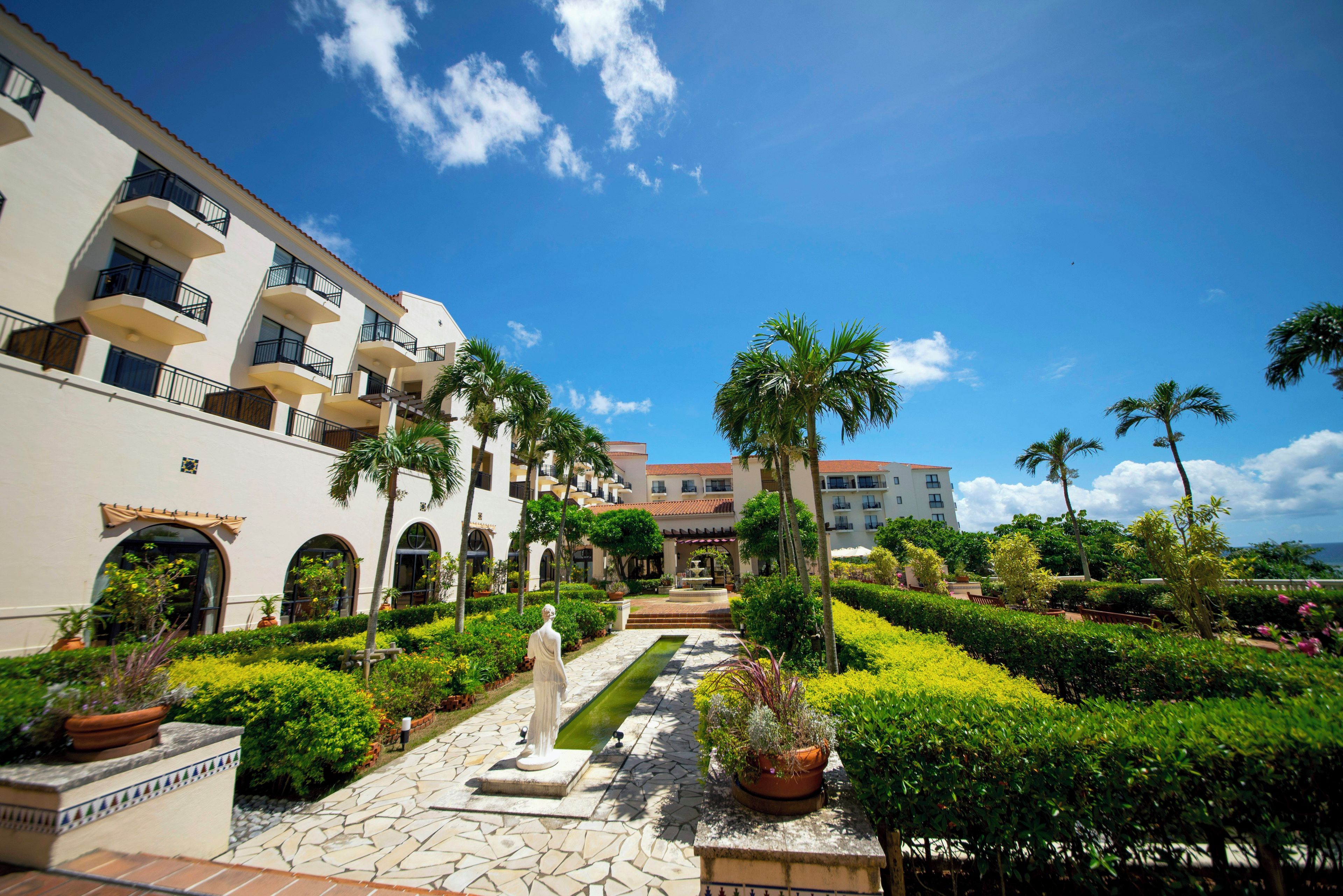 A courtyard with a statue, palm trees, and a pool.