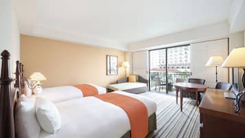 Habitación de hotel con dos camas, un escritorio, una silla y un balcón con vistas a edificios.