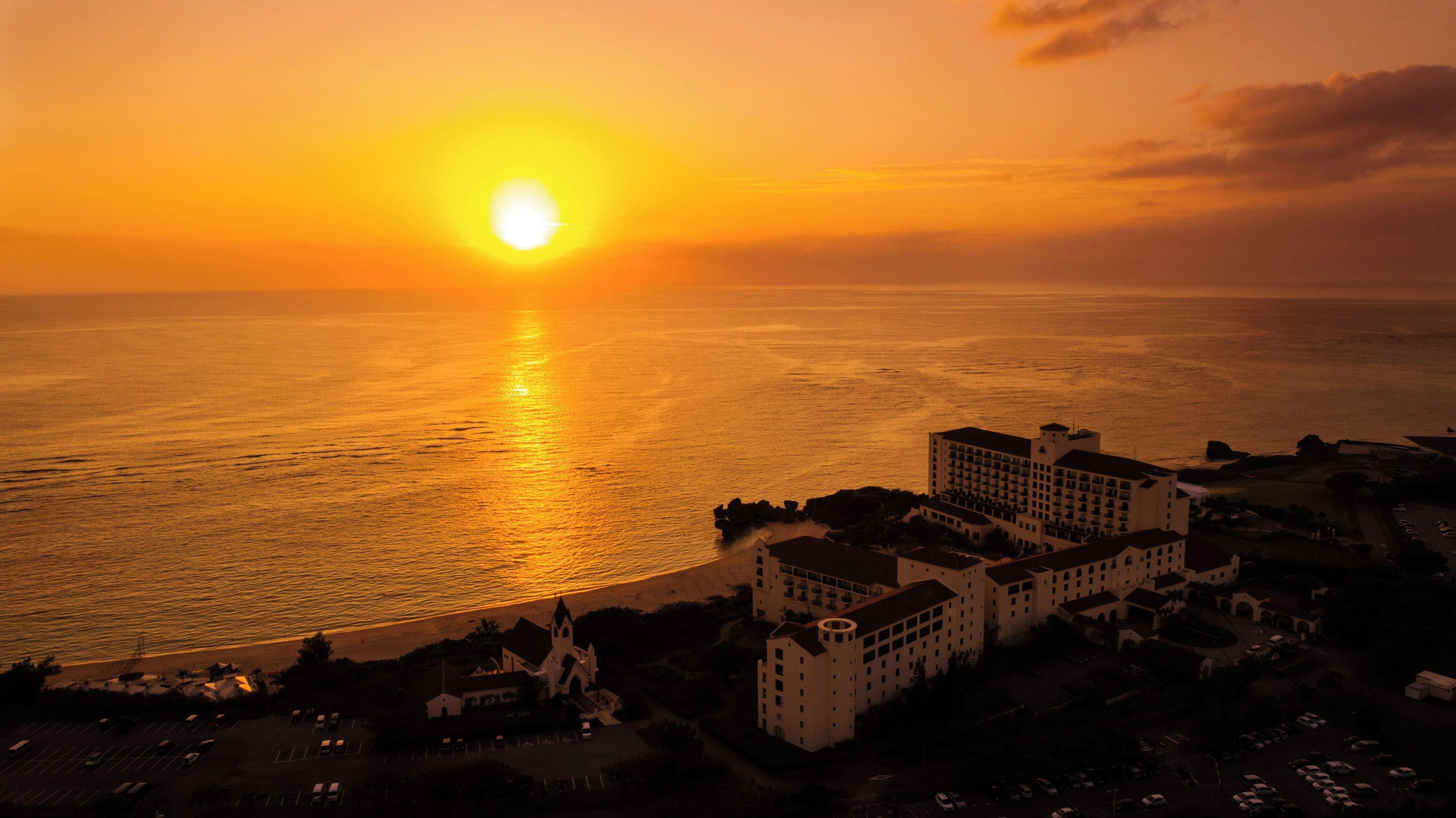 Un hôtel en bord de mer, composé de plusieurs bâtiments, avec une plage et une vue sur le coucher de soleil.