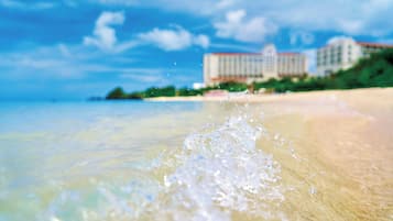 A beach with clear water, a sandy shore, and a building in the background.