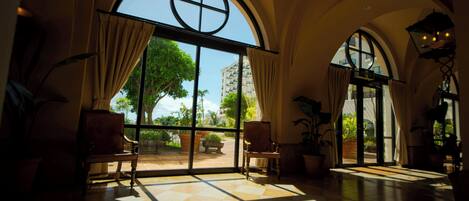 A spacious room with large arched windows, a tiled floor, and several chairs.