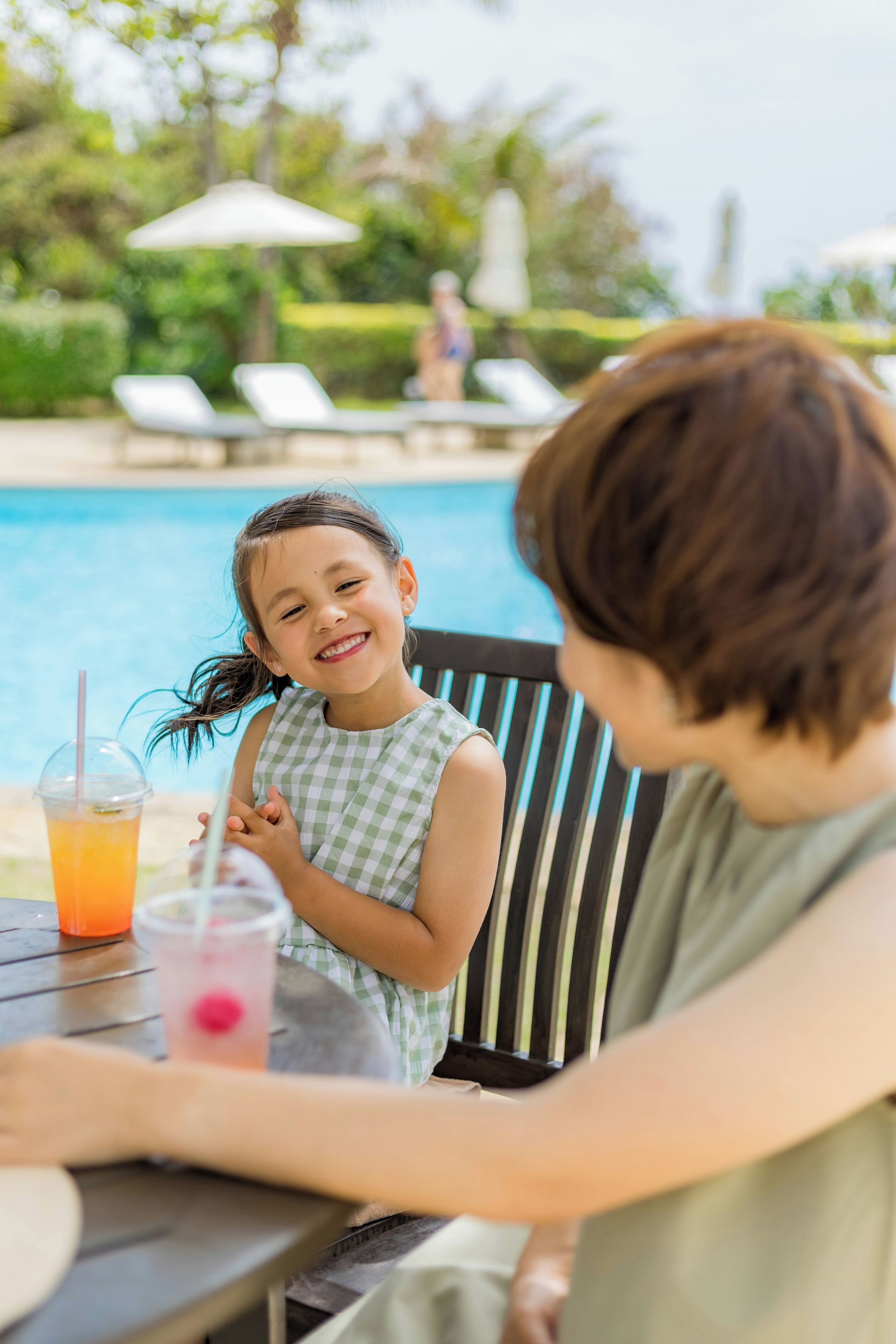 Área de piscina com mesa e cadeiras, vista clara da piscina e uma pessoa sentada à mesa.