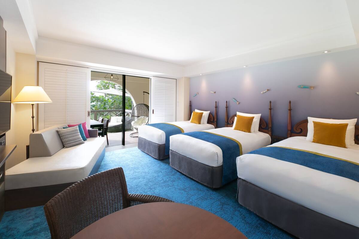 A hotel room with two beds, a sofa, a dining table, and a chair.