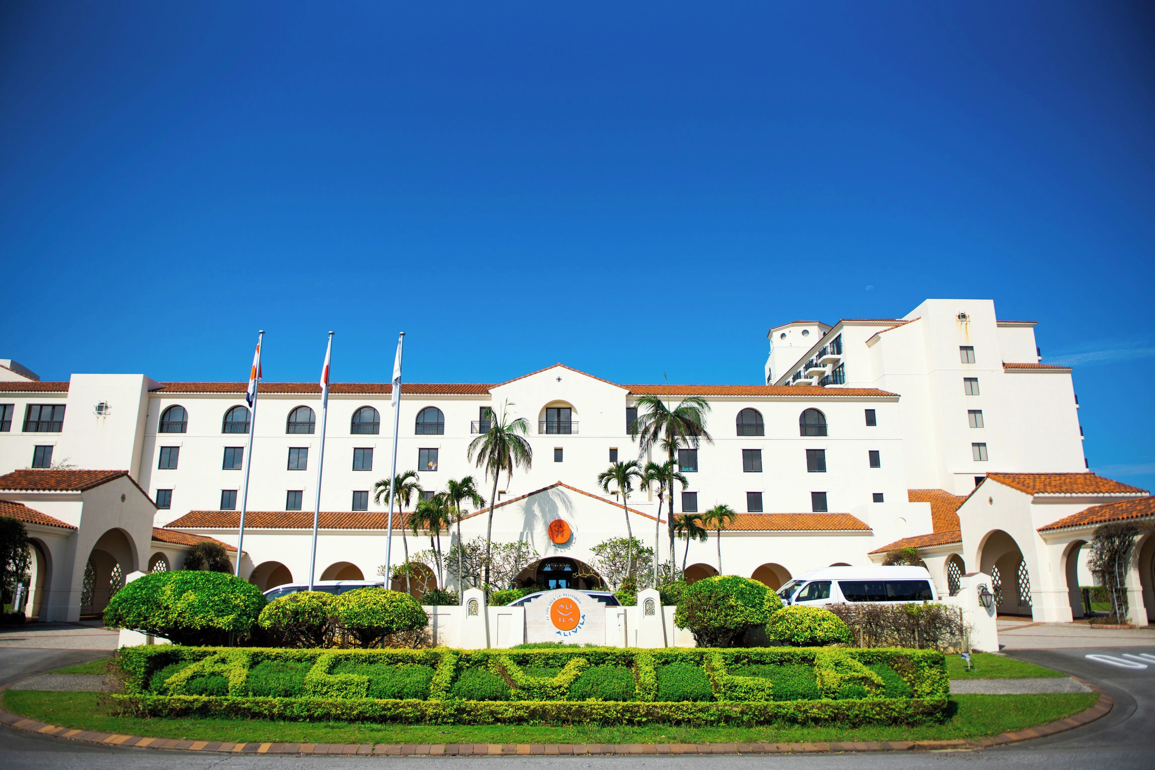 A large hotel with multiple floors, a central courtyard with palm trees, and a clear blue sky.