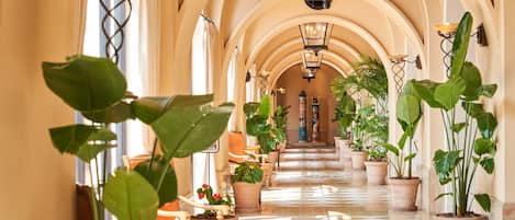 A hallway with arches, potted plants, and a chandelier.